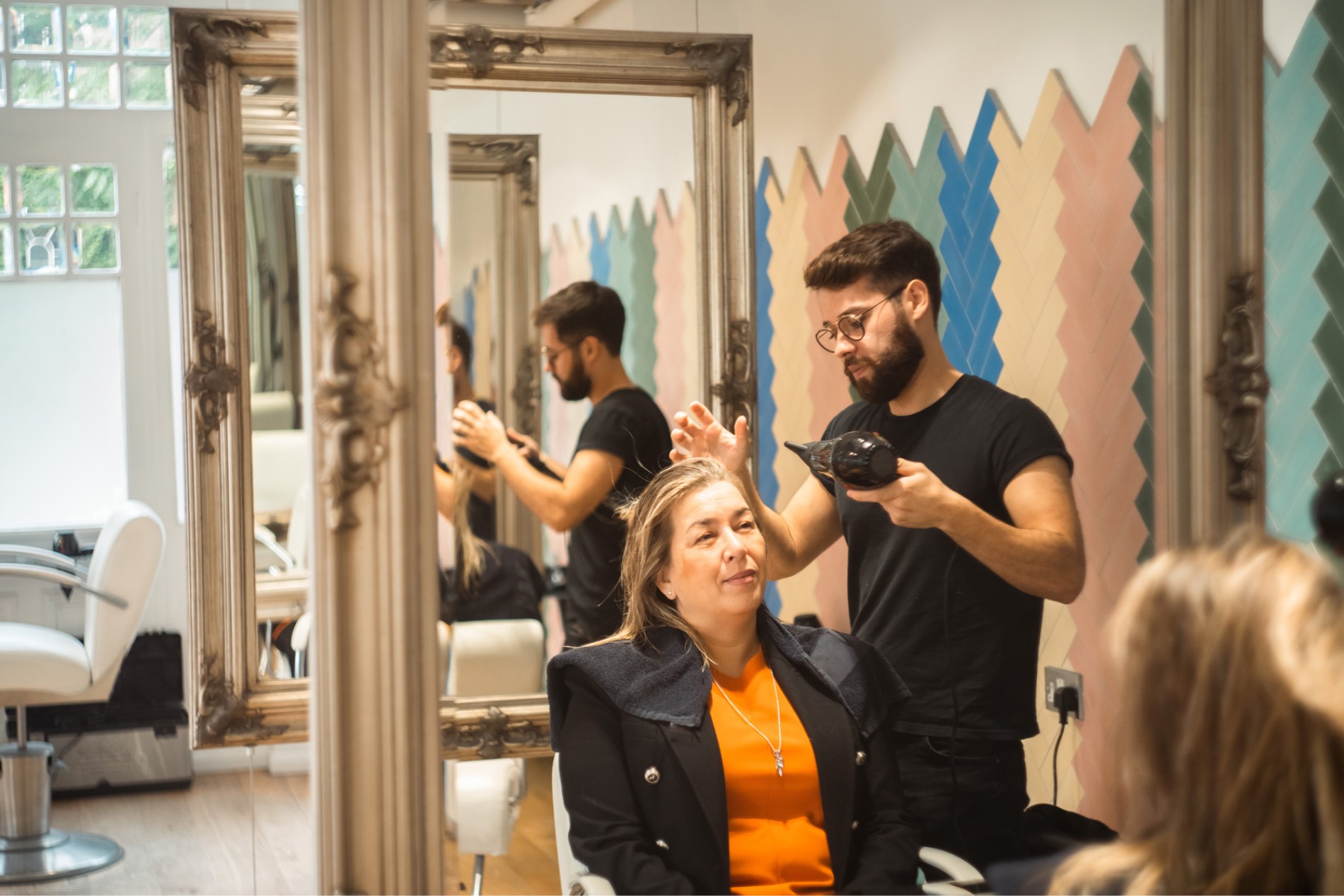 A stylist in front of a mirror, blow drying a guests hair